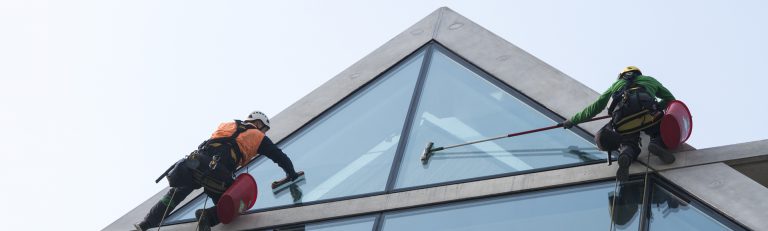 Two window cleaners on rope descent cleaning a glass building peak
